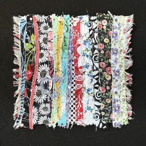 May include: A patchwork textile square composed of vertical strips of fabric in various floral and patterned designs. The strips include daisies, roses, and polka dots, with colors like black, white, red, and blue. The edges are frayed.