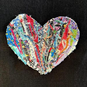 May include: A heart-shaped textile collage constructed from various fabric strips in red, blue, yellow, purple, and green. The piece features a mix of floral, polka dot, and geometric patterns with frayed edges and visible white stitching throughout.