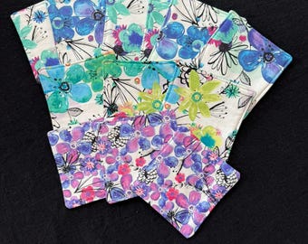 May include: A set of 10 colorful fabric coasters with a floral design. The coasters feature a white background with blue, green, and purple flowers.