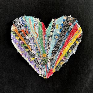 May include: A heart-shaped fabric applique constructed from vertical strips of various patterned textiles including floral, geometric, and solid colors in shades of red, yellow, blue, green, and purple, all held together with white thread.