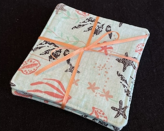 May include: Set of four teal blue fabric coasters with a coral and black floral design. The coasters are tied together with a peach-colored ribbon.