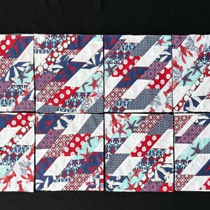 May include: Eight square fabric patches with a nautical theme. Each patch features diagonal stripes in red, white, and blue, with patterns of anchors, lobsters, starfish, and polka dots. The patches are arranged on a black surface.