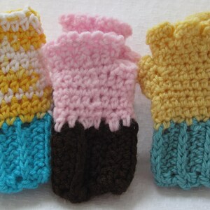 May include: Three pairs of crocheted fingerless gloves in different color combinations. The first pair is yellow and white with a turquoise cuff. The second pair is pink with a brown cuff. The third pair is yellow with a turquoise cuff.