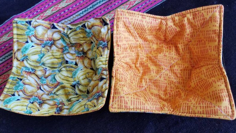 May include: Two square fabric pot holders. One is yellow with a red pattern and the other is yellow with a banana and pumpkin print.