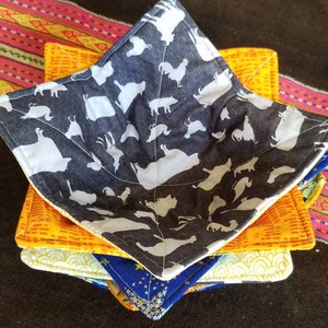 May include: A set of four quilted bowl cozies in various patterns. The top cozy features a black and white pattern of farm animals, the second cozy is orange with a yellow geometric pattern, the third cozy is yellow with a white geometric pattern, and the bottom cozy is blue with a gold star pattern.