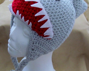 May include: Gray crocheted hat with a red and white felt shark mouth detail. The hat has a long braided cord.