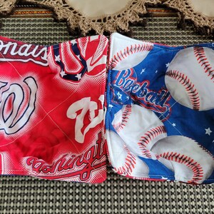 May include: Two red and blue fabric pot holders with baseball and Washington Nationals team logos. The pot holders are quilted and have a white background.