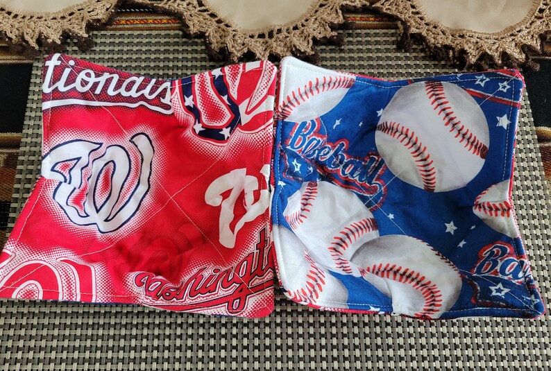 May include: Two red and blue fabric pot holders with baseball and Washington Nationals team logos. The pot holders are quilted and have a white background.