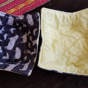 May include: Two quilted bowl cozies. One is black with white animal silhouettes and the other is white with a yellow wave pattern.