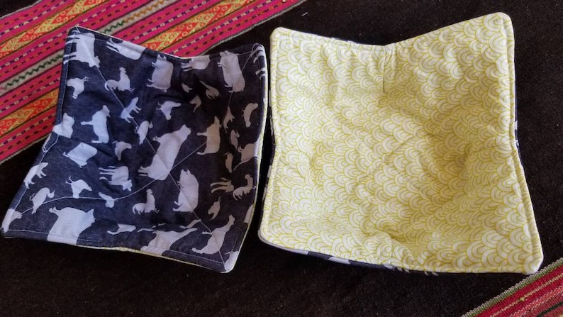May include: Two quilted bowl cozies. One is black with white animal silhouettes and the other is white with a yellow wave pattern.