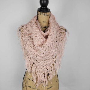May include: A pink crocheted shawl with fringe on a mannequin. The shawl is made of a delicate, open-weave fabric.