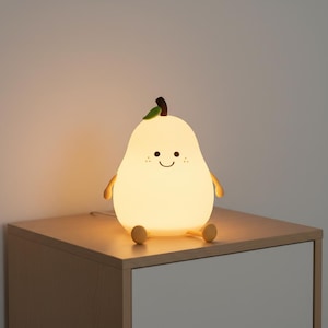 May include: A pear-shaped night light with a smiling face, small arms, and feet. The light is a soft yellow color, with a green leaf and brown stem. It sits on a light-colored wooden nightstand.