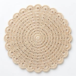May include: A round, beige crochet doily with a scalloped edge. The doily is made of a natural fiber and features a detailed, concentric circle design. This handmade item is perfect for adding a touch of rustic charm to any home decor.