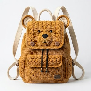 May include: A mustard yellow crochet backpack shaped like a bear, featuring a bear face on the flap, two small pockets, and adjustable straps. The backpack has a drawstring closure and wooden button details.