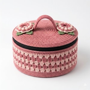 Puede incluir: Una caja de almacenamiento redonda de ganchillo rosa, con asa y cremallera negra. La tapa está adornada con dos aplicaciones de flores de ganchillo. Los lados presentan un diseño estampado en tonos rosas y blancos. Para objetos pequeños.