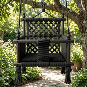 May include: A black wooden swing with a macramé back and seat, suspended from a tree branch. The swing features a woven design and decorative tassels. The swing is designed for outdoor use.