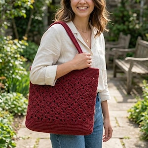 May include: A deep red crochet tote bag featuring a textured diamond pattern and a solid base. The bag has a single shoulder strap and is crafted from yarn with a consistent stitch design throughout the body of the accessory.
