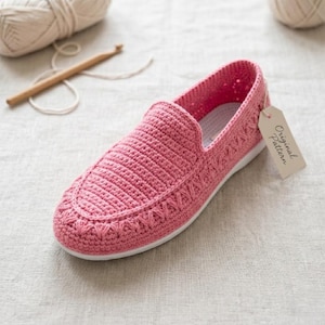 Op de afbeelding: Een roze gehaakte loafer-schoen met een witte zool. De schoen heeft een textuurontwerp en een label met de tekst "Original Pattern". Garen en een haaknaald staan op de achtergrond.