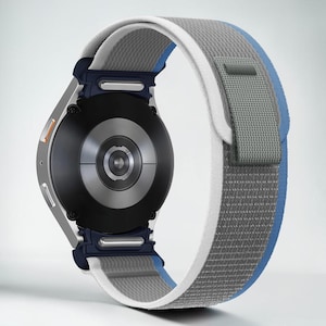 May include: A silver smartwatch with a black face and a gray, white, and blue fabric band. The watch has a dark blue attachment piece and an orange button. The band is secured with a gray loop.