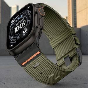 Puede incluir: Un reloj inteligente negro con pantalla digital que muestra la hora, la temperatura y datos de ubicación. El reloj cuenta con una correa de nailon verde oliva texturizada con una costura en zigzag naranja cerca de la caja y una hebilla negra.