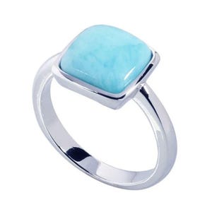 May include: A polished silver ring featuring a square-shaped, light blue stone with a smooth, marbled surface. The setting is a simple, clean metal band that holds the stone securely in a raised, four-sided frame, creating a bright, reflective look.