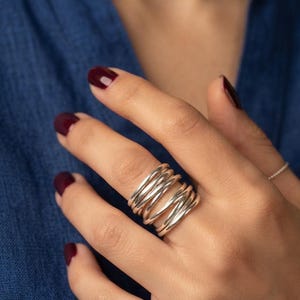 Op de afbeelding: Een ring met meerdere banden gemaakt van gepolijst zilverkleurig metaal, bestaande uit verschillende dunne, afgeronde draadringen die elkaar overlappen en in een doorlopend, gelaagd spiraalpatroon om de vinger wikkelen voor een brede uitstraling.