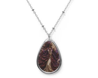 Op de afbeelding: Een zilverkleurige druppelvormige hanger aan een ketting met een gedetailleerde illustratie van een figuur in een vloeiend paars en wit gewaad met een hoofddoek. De hanger hangt aan een fijne zilveren ketting met kleine, gelijkmatig verdeelde metalen kralen.