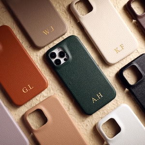 Può includere: Una collezione di cover per telefono testurizzate in vari colori, tra cui verde scuro, nero, marrone, beige e lavanda. Ogni cover presenta un ritaglio per la fotocamera e iniziali dorate in rilievo come W.J, K.F, G.L, A.H e D.