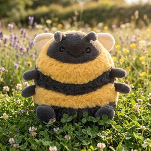 May include: A plush bee toy with a round body, featuring yellow and black stripes. The bee has small, gray arms and legs, with a smiling face and small antennae. The toy is set in a field of green grass and wildflowers.