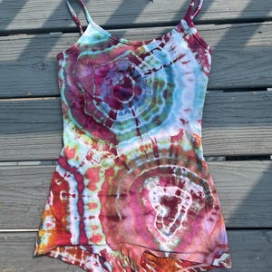 May include: A sleeveless romper featuring a vibrant tie-dye pattern in shades of magenta, teal, orange, and white. The garment has thin spaghetti straps, a scoop neckline, and a fitted silhouette that extends into short leg openings.