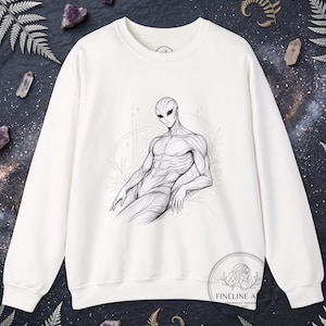 Könnte beinhalten: Cremefarbenes Sweatshirt mit einer Schwarz-Weiß-Illustration eines Außerirdischen. Das Kunstwerk zeigt detaillierte Linien und Schattierungen, die den Außerirdischen in einer entspannten Pose zeigen. Das Sweatshirt hat einen Rundhalsausschnitt und lange Ärmel. Design von Fineline Art.
