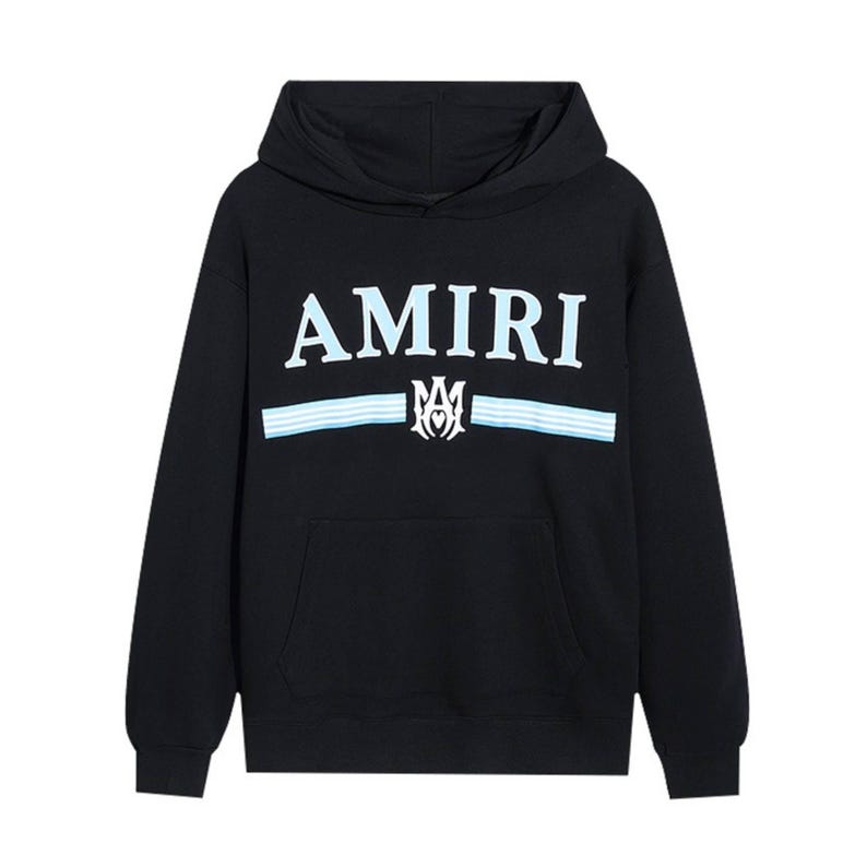 May include: Black hooded sweatshirt with the word "AMIRI" in white and light blue lettering across the chest. Below the word "AMIRI" are two light blue stripes and a white emblem. The sweatshirt has a front pocket.