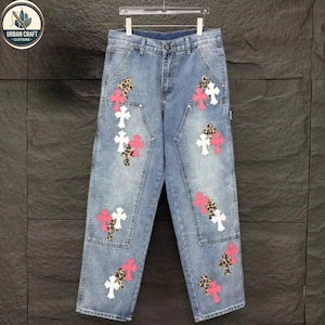 May include: Light blue denim jeans with multiple cross and leopard print patches. The jeans are hanging on a hanger. The Urban Craft Clothing logo is in the upper left corner.