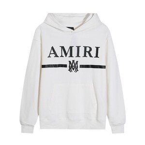 May include: White hoodie with a front pocket and a hood. The word "AMIRI" is printed in black across the chest, above a black horizontal stripe and a decorative emblem.