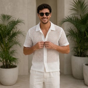 Peut inclure: Une chemise blanche à manches courtes boutonnée avec un motif en maille crochetée à grille carrée, un col classique et une fermeture frontale boutonnée. La chemise est associée à un pantalon clair, formant un ensemble coordonné texturé.