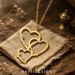 May include: A gold-toned necklace featuring a pendant composed of three interconnected heart outlines. Each heart frame incorporates a name engraved in a cursive script, specifically the names Aleacus, Alyuta, and Jeason, suspended from a chain.