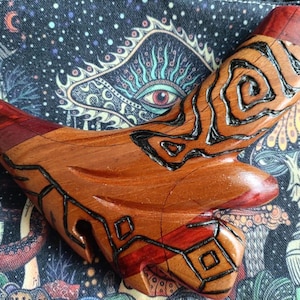 May include: A handcrafted wooden pipe with a unique, organic shape. The pipe features a combination of light and dark wood tones, with intricate black line detailing. The design includes geometric and swirling patterns, creating a distinctive aesthetic.