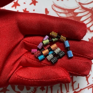 May include: A collection of small, colorful metal components with threaded black centers. The components are in various colors, including red, blue, green, and silver. The items are held in a red glove.