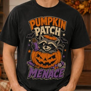 May include: A black short-sleeve t-shirt featuring a graphic of a raccoon sitting inside a carved jack-o'-lantern pumpkin. The text reads PUMPKIN PATCH MENACE in orange and purple letters, surrounded by small bats, stars, and candy illustrations.