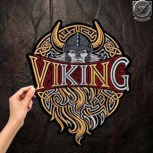 May include: A circular embroidered patch featuring a central Viking warrior wearing a horned helmet, surrounded by intricate gold and silver Celtic knotwork. The word VIKING is stitched in large, bold, gold and silver letters across the centre.