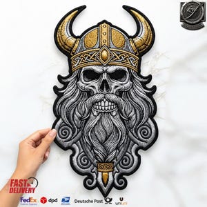 Puede incluir: Un parche bordado que presenta una calavera con un casco vikingo con cuernos. El diseño utiliza hilo dorado, plateado y negro para representar una calavera detallada con una barba larga y fluida y patrones de nudos intrincados en la banda del casco.