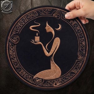May include: A circular black embroidered patch featuring a copper-colored silhouette of a kneeling figure holding a lit candle with rising smoke. The design is enclosed within a decorative border of geometric patterns and a crescent moon symbol.