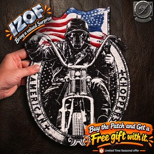 May include: A black and white embroidered patch featuring a skull wearing a helmet, riding a motorcycle, set against a background of the American flag. The oval border includes the text AMERICAN CHOPPERS and decorative fleur-de-lis symbols.