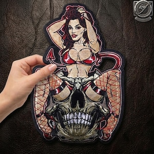 Può includere: Una toppa ricamata raffigurante una figura di diavolessa con lunghi capelli scuri e piccole corna, che indossa un top bikini rosso. La figura è seduta sopra un grande teschio umano e indossa calze a rete. Il design include una coda rossa.