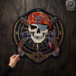 May include: A circular embroidered patch featuring a skull wearing a red bandana with a sextant and eye patch, crossed flintlock pistols, and a compass rose background with a rope border and an anchor at the bottom, with N, W, and E letters.