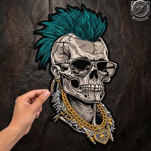 May include: An embroidered patch featuring a skull with a vibrant teal mohawk hairstyle, wearing black-rimmed sunglasses. The skull is adorned with a thick gold-colored chain necklace that features a heart-shaped pendant with a small skull design.