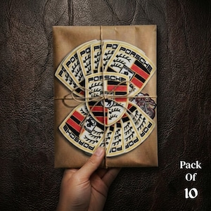 May include: A pack of 10 Porsche logo patches, featuring the Porsche crest in red, black, and gold, arranged on a brown paper-wrapped package tied with twine. The text "Pack Of 10" is visible.