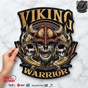 Puede incluir: Un parche bordado negro que muestra tres calaveras con cascos vikingos con cuernos, con el texto VIKING WARRIOR en letras doradas. La calavera central tiene barba y dos hachas cruzadas se sitúan detrás de las calaveras sobre un fondo negro.