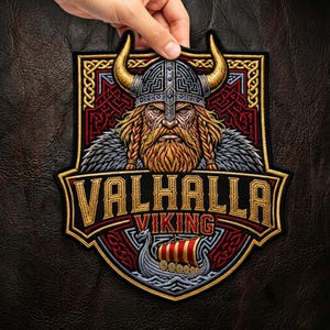 May include: A shield-shaped embroidered patch featuring a bearded Viking warrior wearing a horned helmet. Below the warrior, the text reads VALHALLA VIKING in gold and red lettering, positioned above a stylised longship with a red and gold sail.