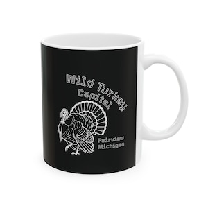 May include: White ceramic mug with a black background featuring a white illustration of a turkey and the text "Wild Turkey Capital" and "Fairview Michigan". The mug has a white handle and interior.